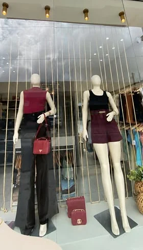 Vitrine da Oly Store Premium com dois manequins e bolsas vinho.