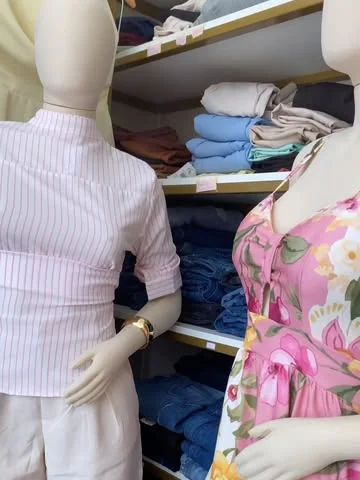 Vestido floral rosa de alça ao lado de camisa listrada rosa, nos manequins da loja.
